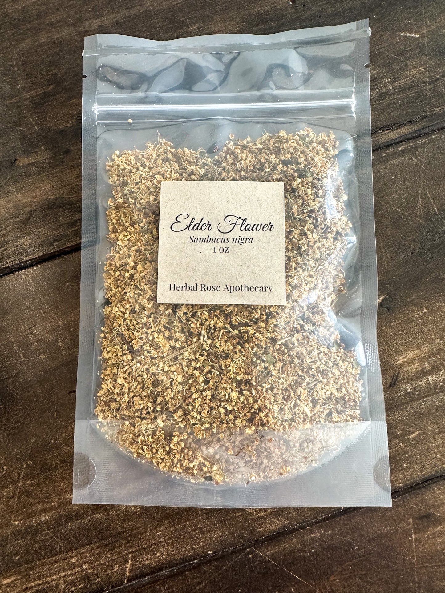 elder flowers packaged in a clear 1oz bag from herbal rose apothecary on a wooden surface