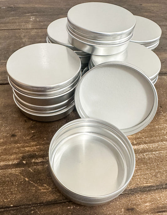 A set of empty round silver aluminum tins with screw-on lids, arranged on a rustic wooden surface.