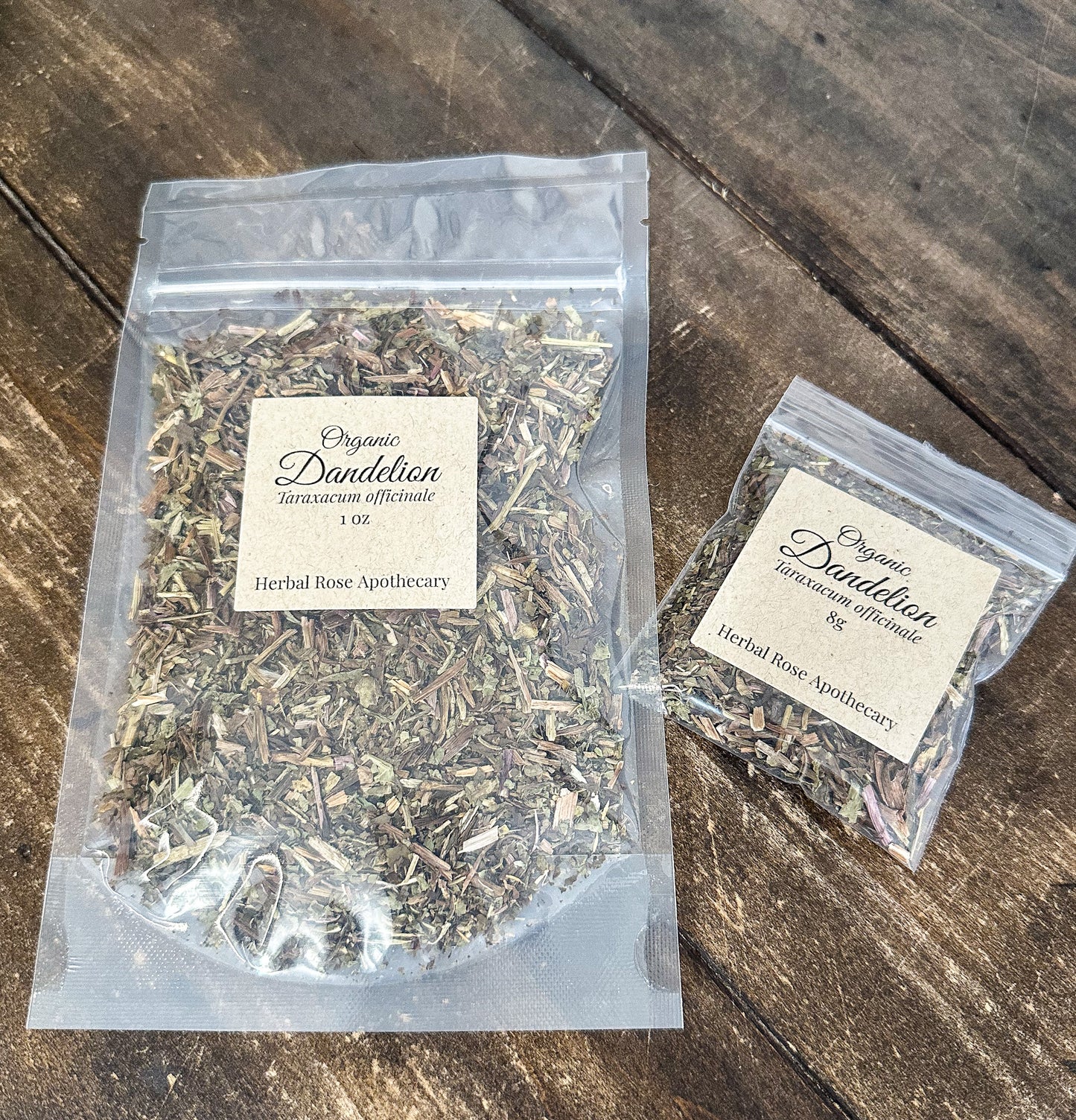Two clear plastic bags of Organic Dandellion by herbal rose apothecary on a rustic dark wood surface.