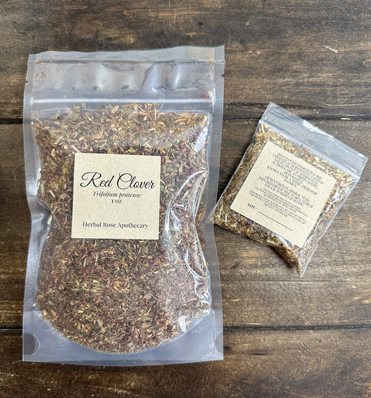 two packages of dried red clover leaves in clear resealable bags from herbal rose apothecary on a wooden surface