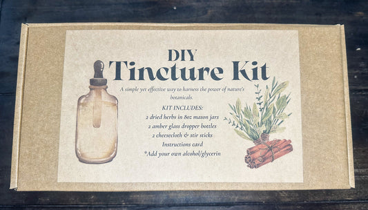 DIY Tincture Kit in a square kraft paper box with a large cream-colored front label. The label features an illustration of a glass dropper bottle, text detailing the kit contents, and an illustration of green herbs and cinnamon sticks.