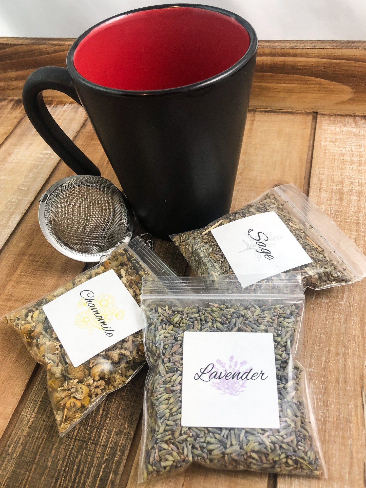 8g clear plastic bags of dried lavender, sage, and chamomile next to a black mug on a wooden background