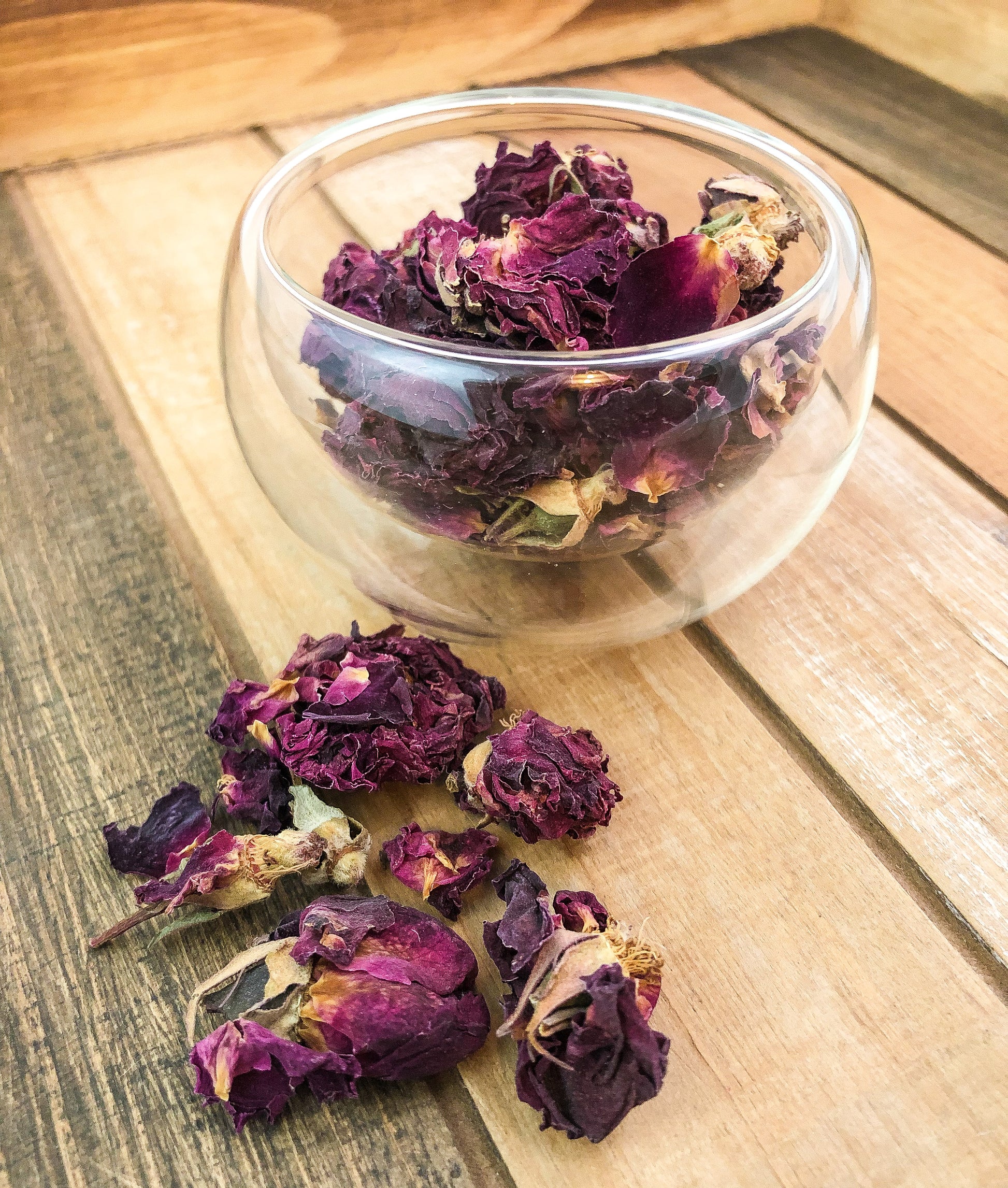 rose petals in a glass cup on a wooden tray