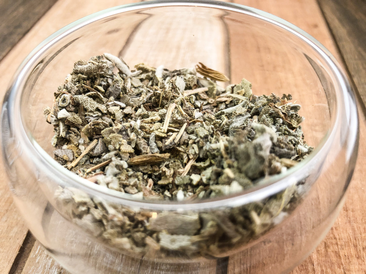 upclose image of dried sage in a small clear glass cup with wooden table as background