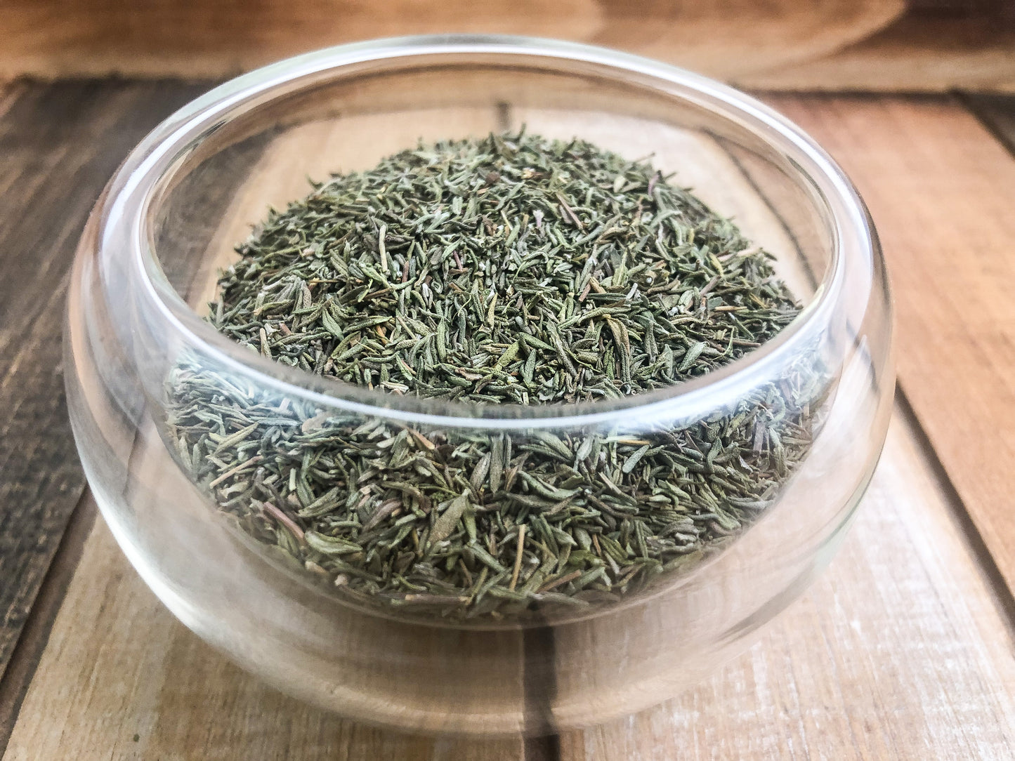 dried thyme in a small clear glass cup on a wooden table as background
