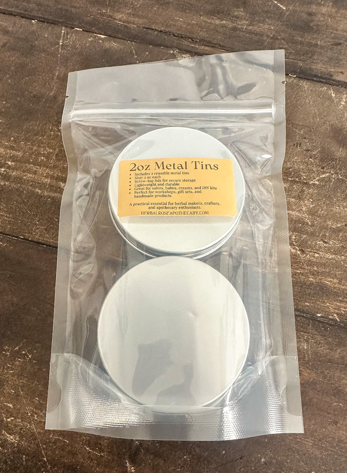 2 pack of 2oz metal tins packaged into a clear bag on a wooden surface