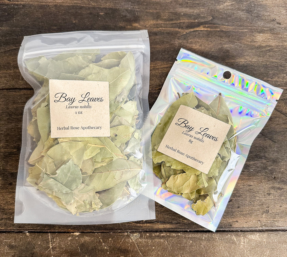 two packages of bay leaves 1oz and 8g bags from herbal rose apothecary on a wooden surface