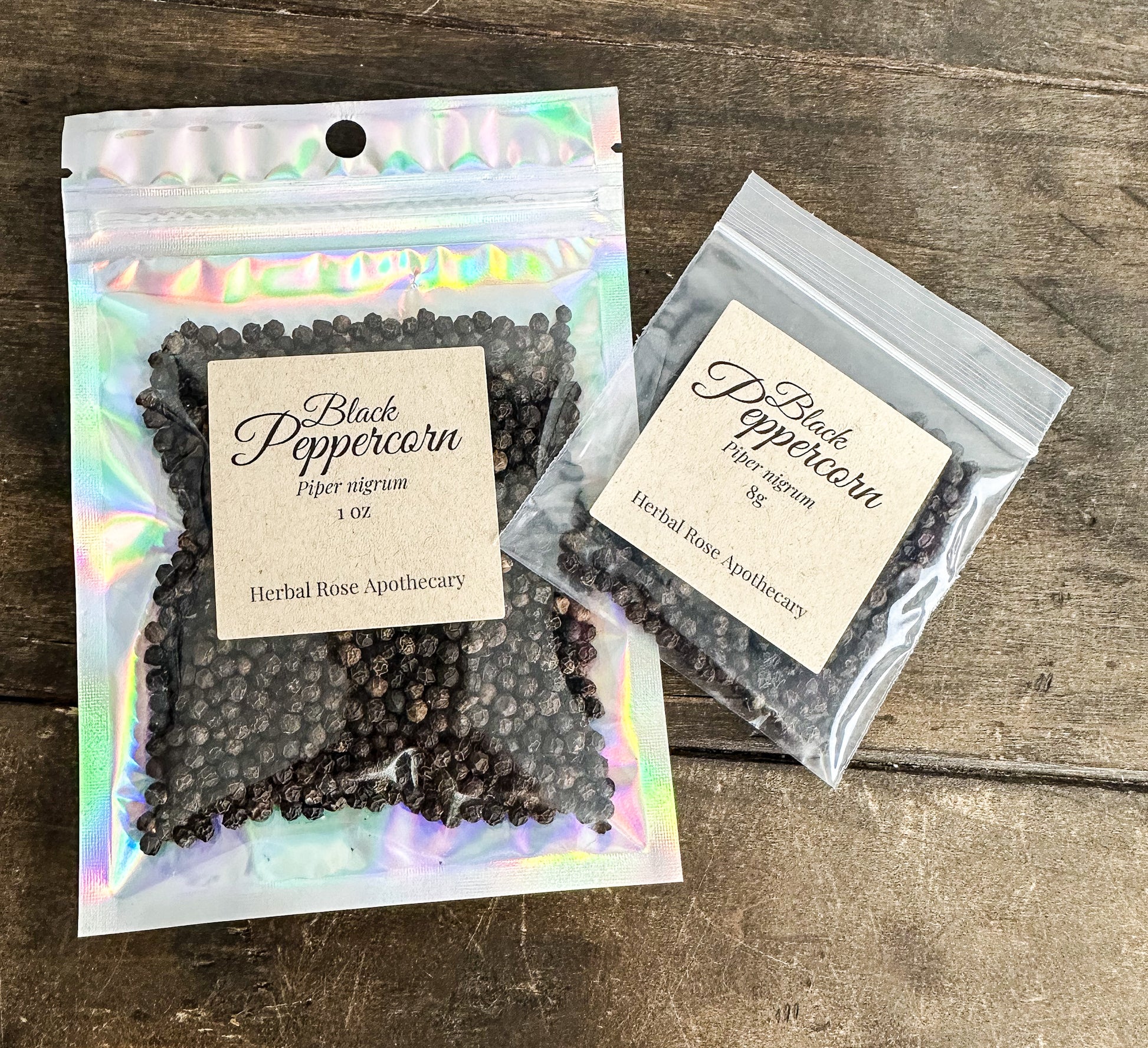 Two packages of Black Peppercorn from Herbal Rose Apothecary on a wooden surface.