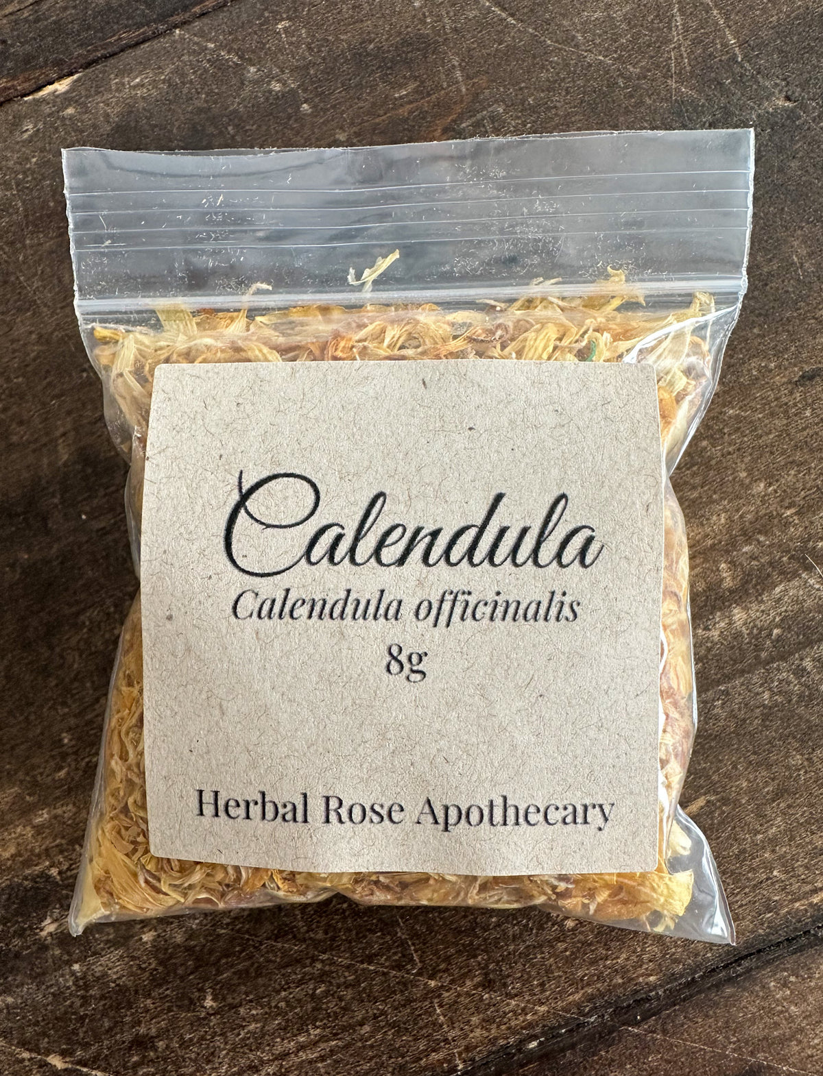 Packaged calendula 8g bag of herbs with a label on a wooden surface