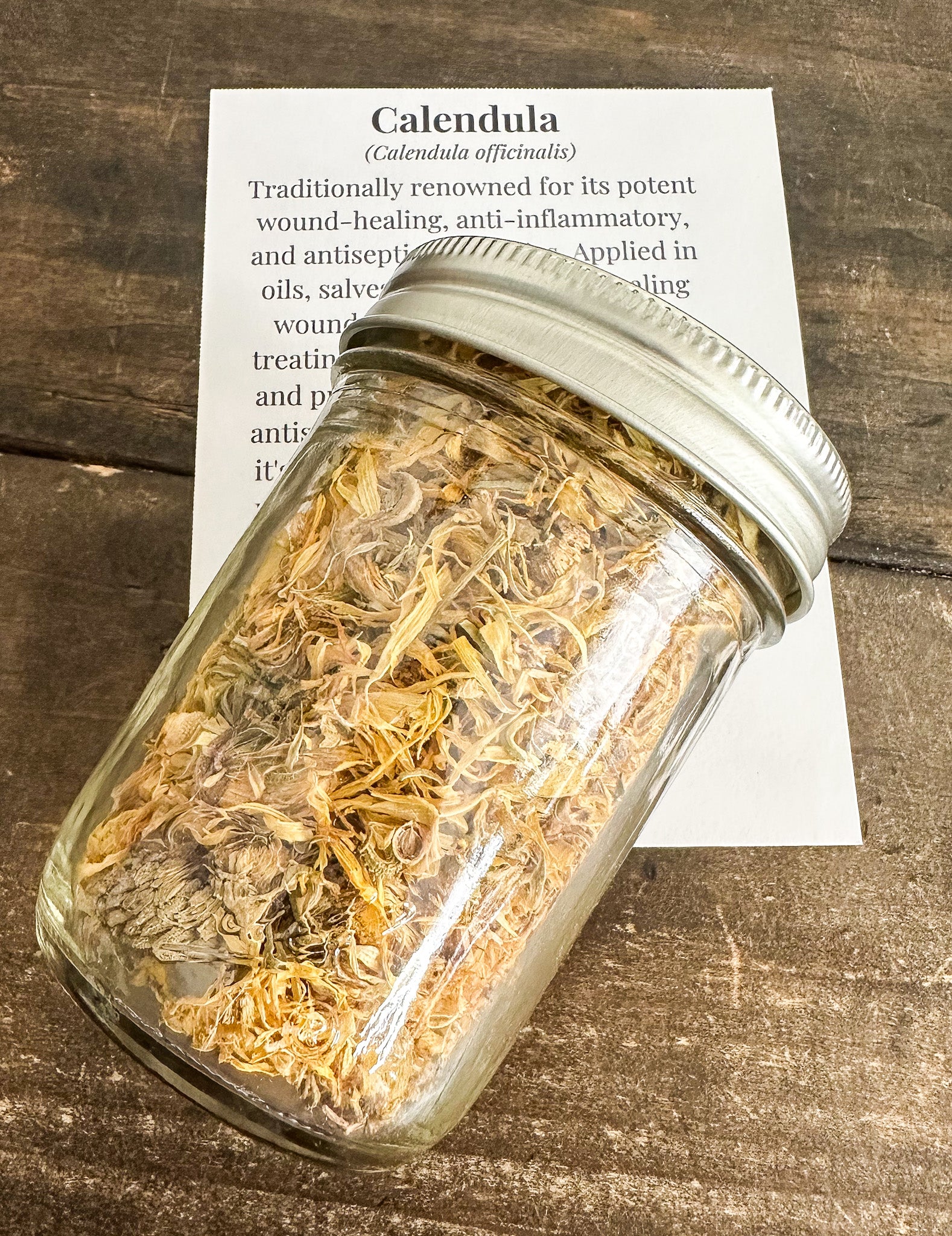 dried calendula in a 8oz mason jar lying on top of a monograph card for calendula