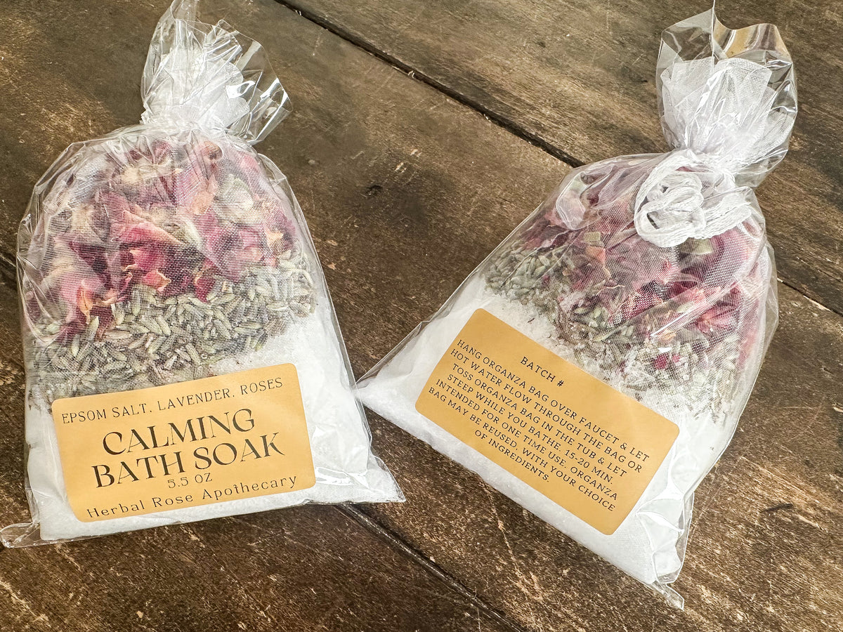two calming bath soaks packaged in a clear bag and labeled lying on a wooden surface from herbal rose apothecary