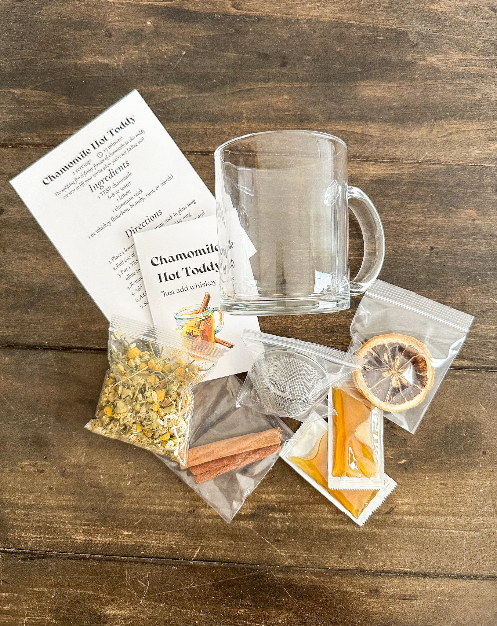 chamomile hot toddy tea-making kit with clear mug, tea bags, and recipe card on wooden surface