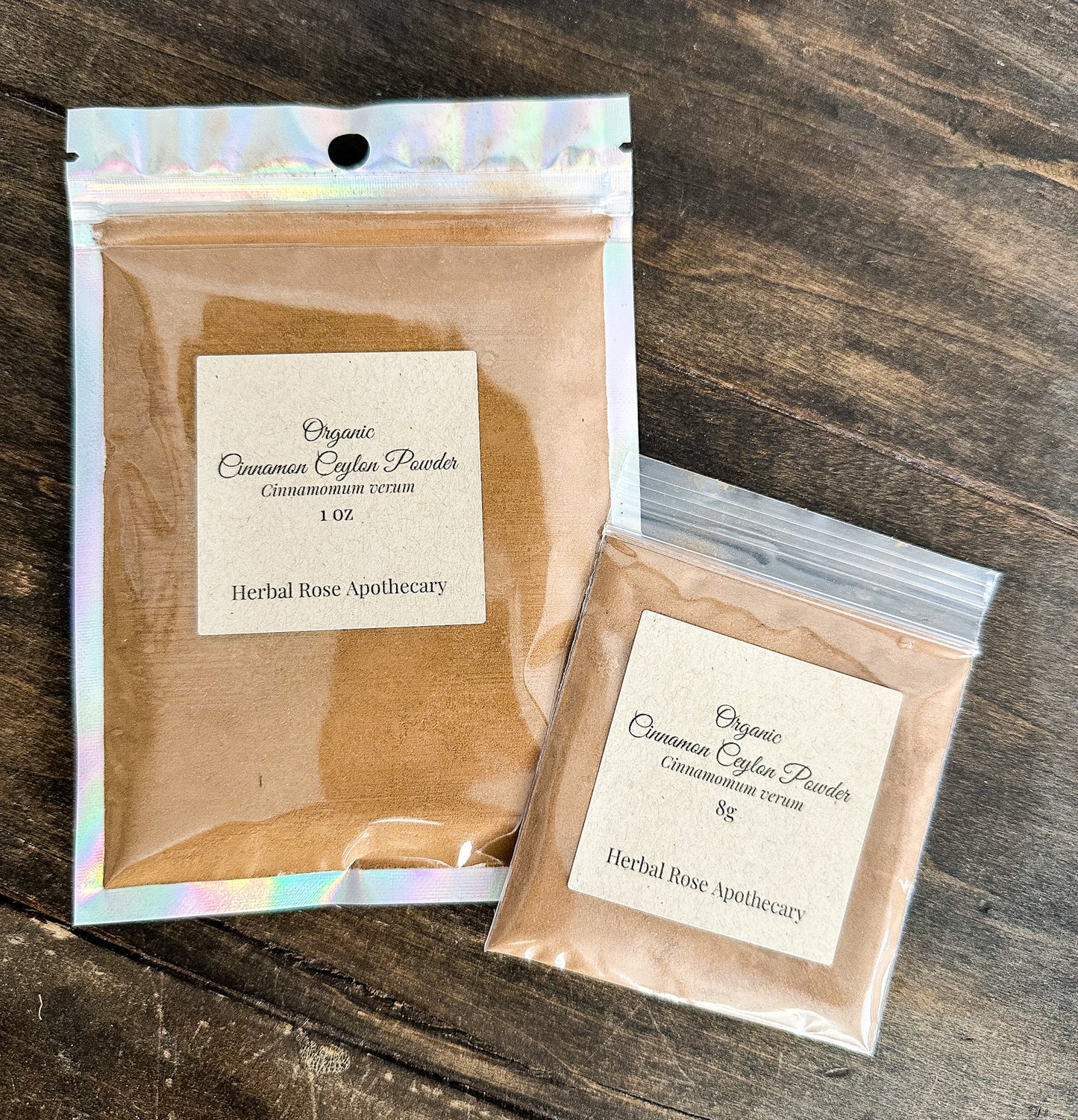 Two packages of Organic Cinnamon Cayenne Powder from Herbal Rose Apothecary on a wooden surface.
