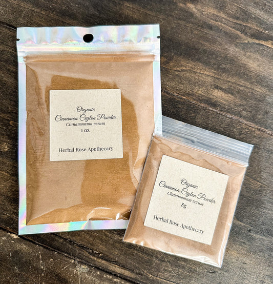 Two packages of Organic Cinnamon Cayenne Powder from Herbal Rose Apothecary on a wooden surface.