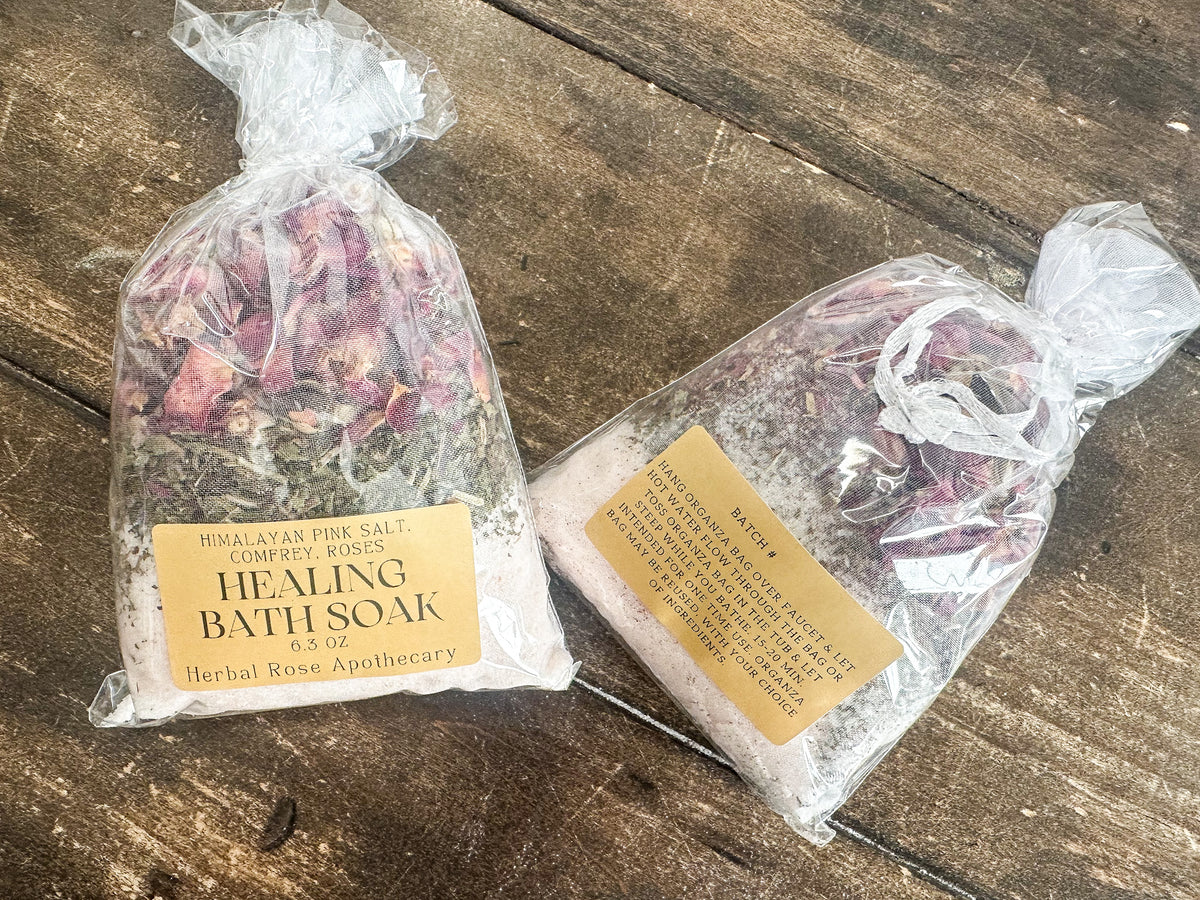 two healing bath soak packaged in a clear bag and labeled lying on a wooden surface from herbal rose apothecary