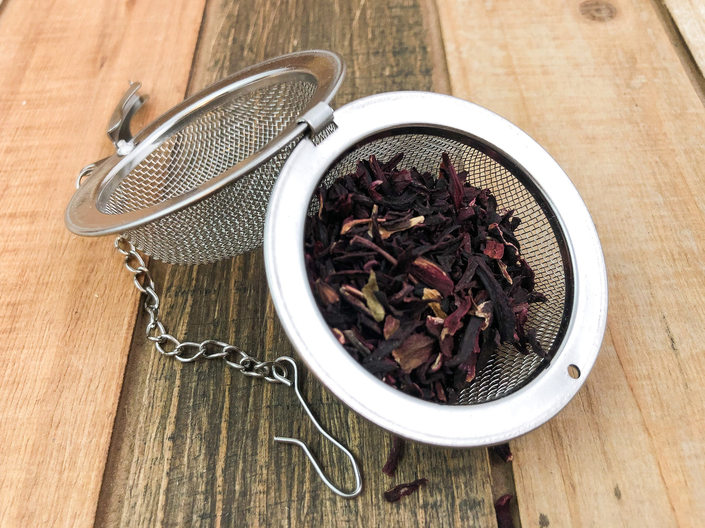 dried hibiscus leaves in an open tea ball infuser on a wooden surface