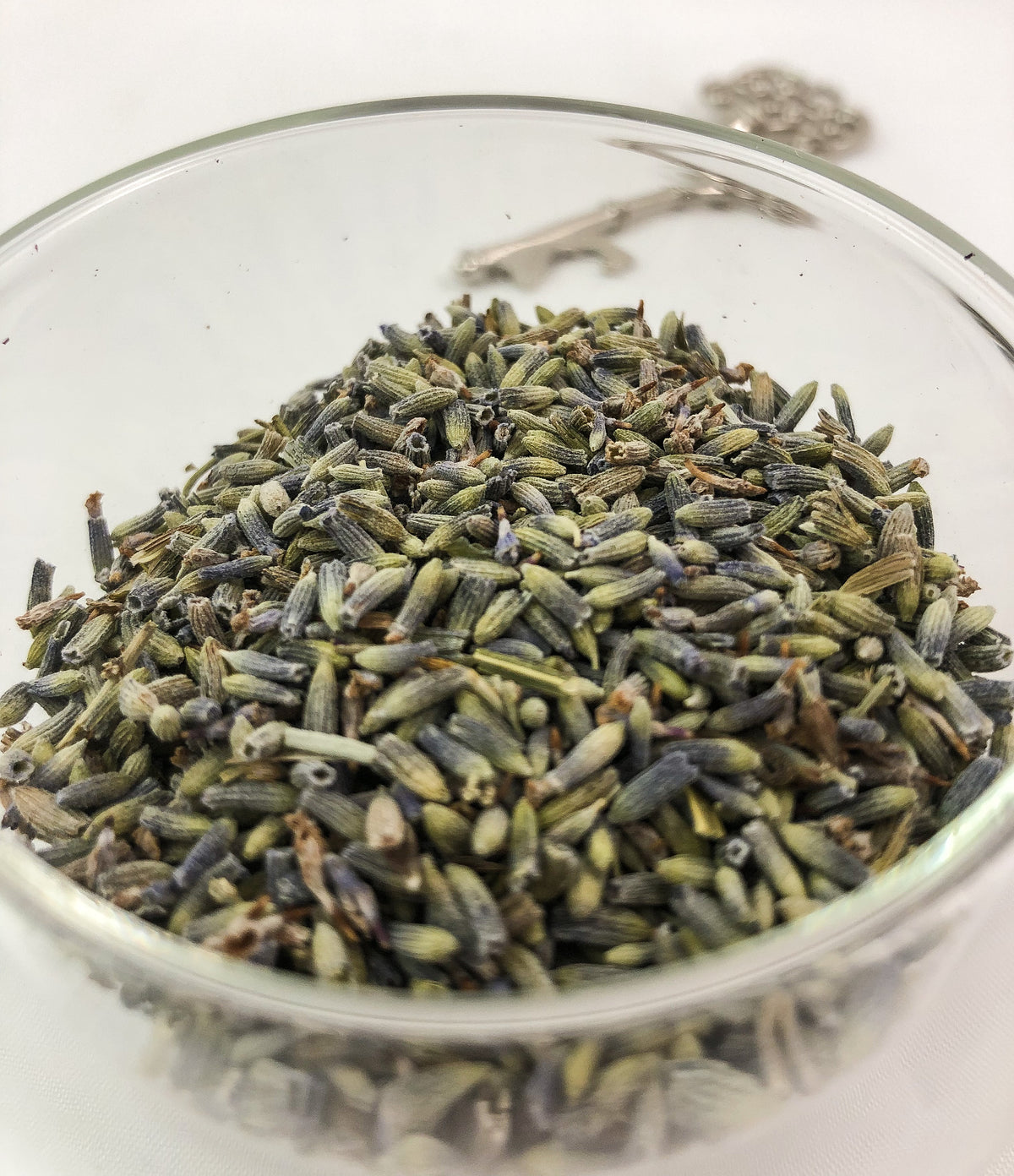 dried lavender buds up close in a clear glass jar showing the green and purple coloring on buds with a white background and key in the background