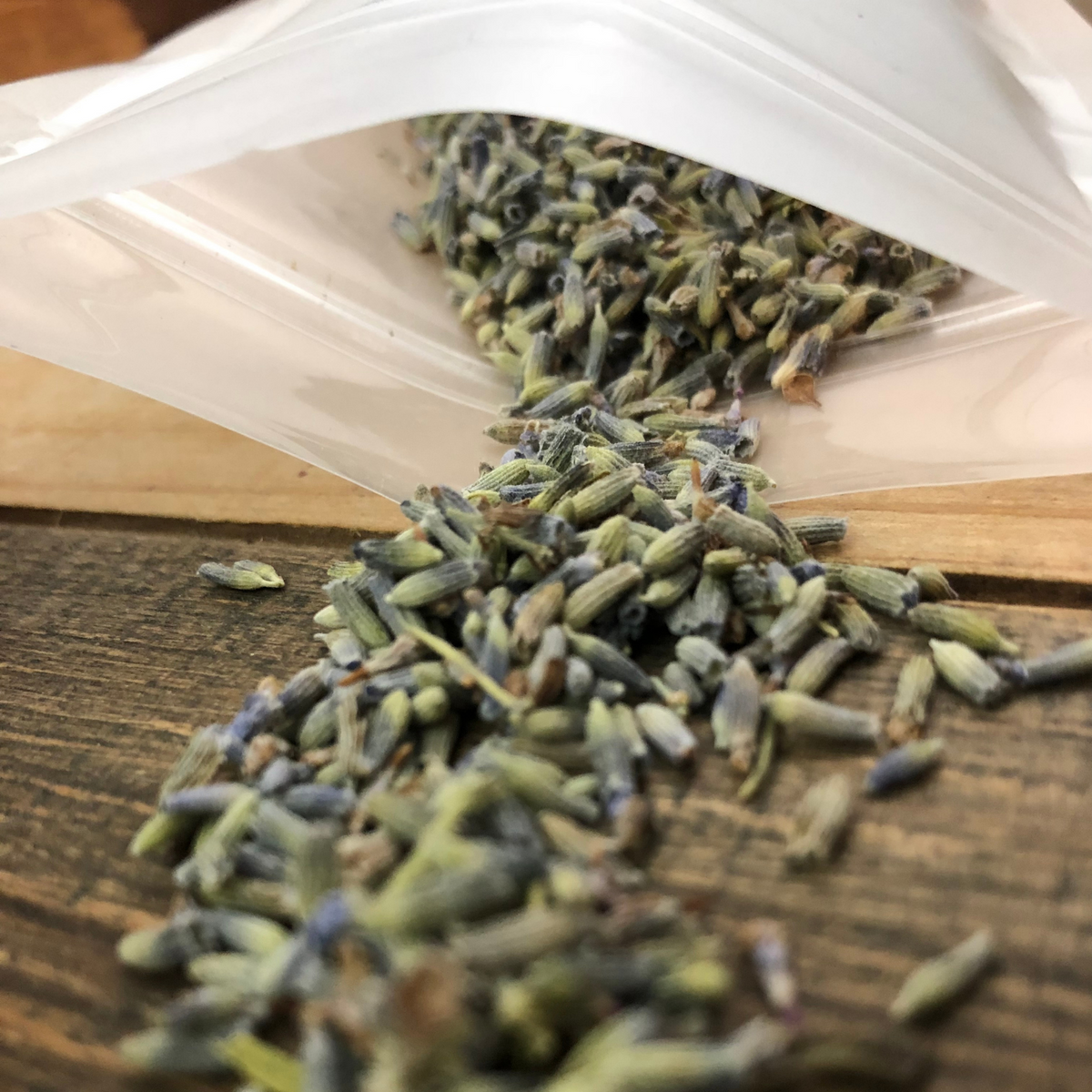 dried lavender buds up close image showing buds of purple and green on a wooden surface spilling out of a opaque bag