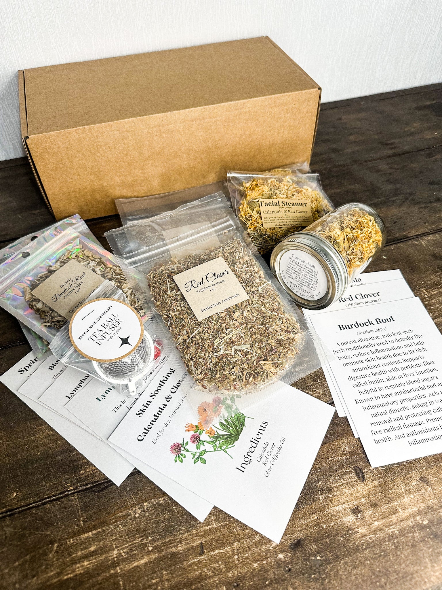 march subscription box red clover, burdock root, calendula and recipe cards, monograph cards and facial steamers with calendula & red clover on a wooden table