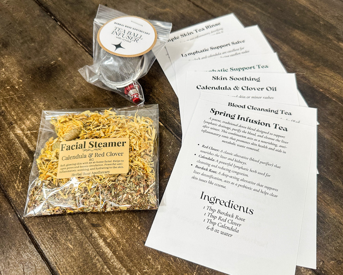 recipe cards laid out on wooden table along side a packaged tea ball infuser and facial steamer