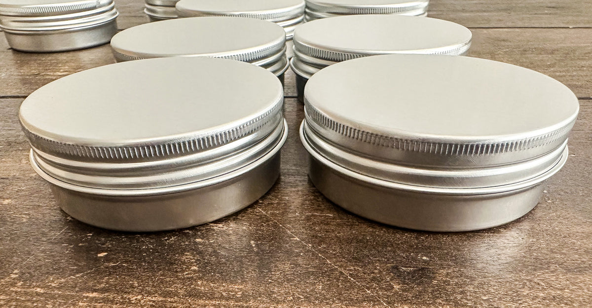 Stacks of round silver metal tins with screw-top lids, arranged on a dark brown wooden surface.