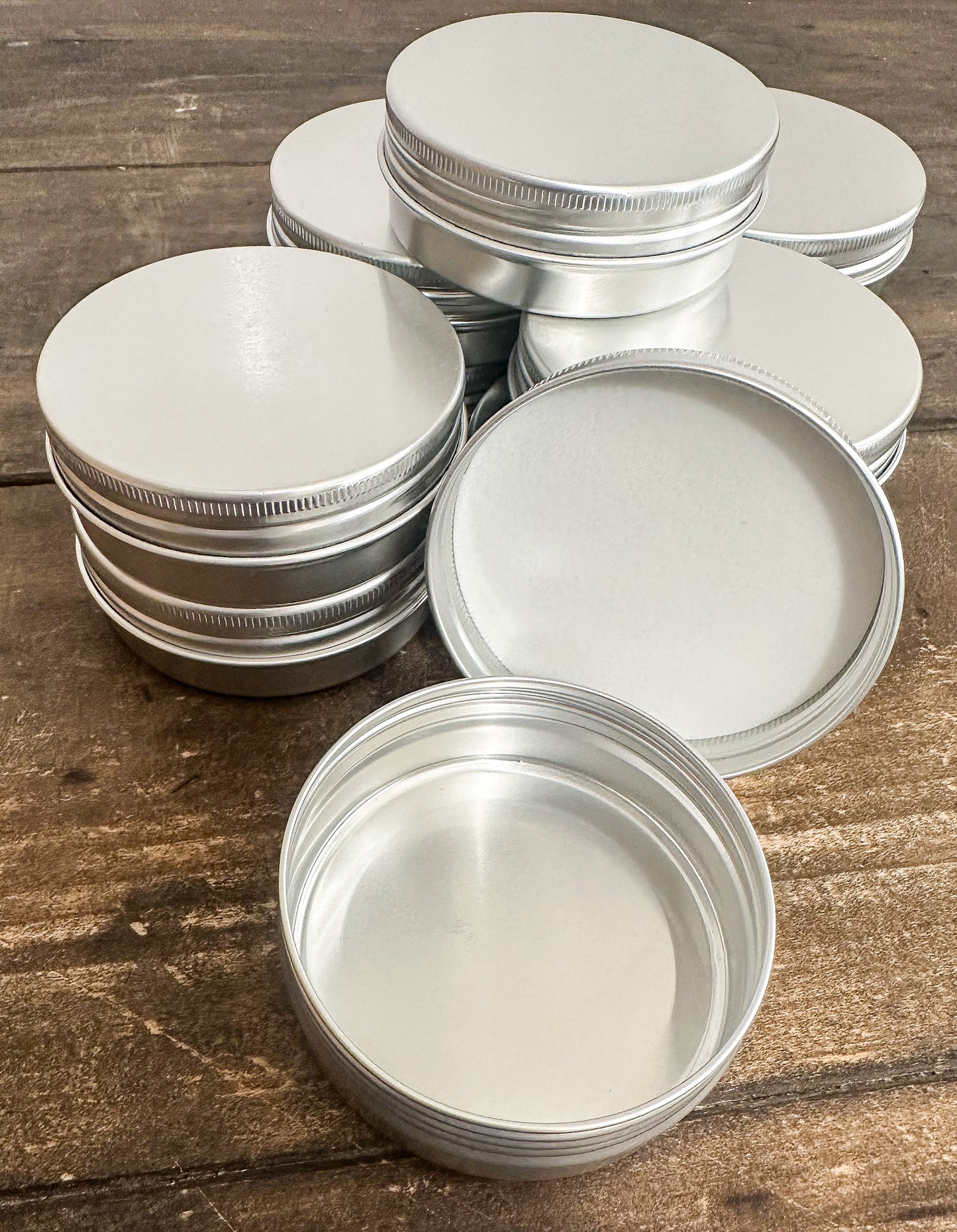 A set of empty round silver aluminum tins with screw-on lids, arranged on a rustic wooden surface.