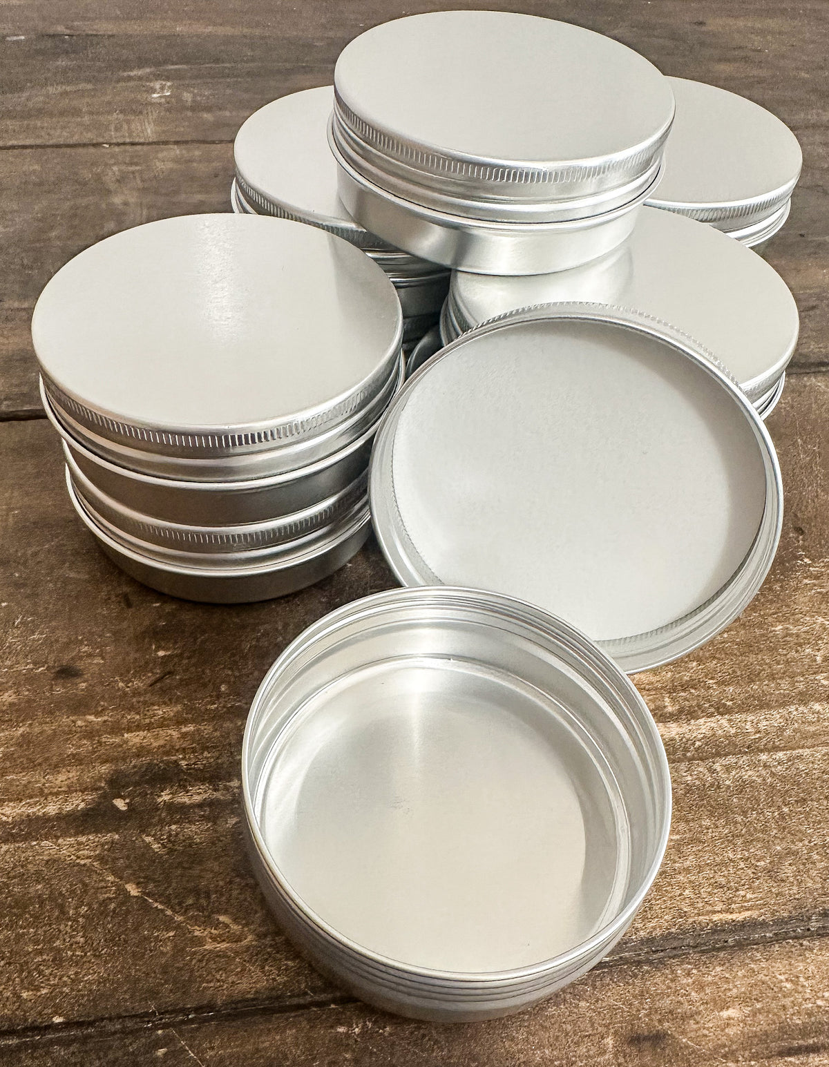 A set of empty round silver aluminum tins with screw-on lids, arranged on a rustic wooden surface.