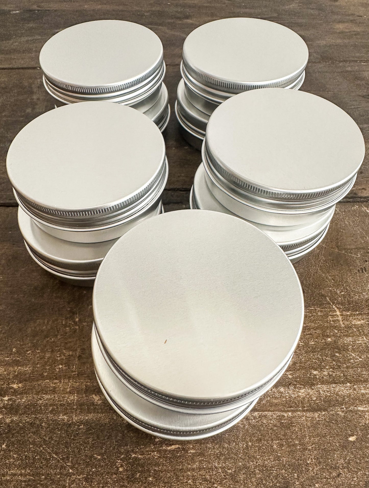 Six stacks of round silver metal tin lids with ribbed screw-on edges, arranged on a dark brown wooden surface.