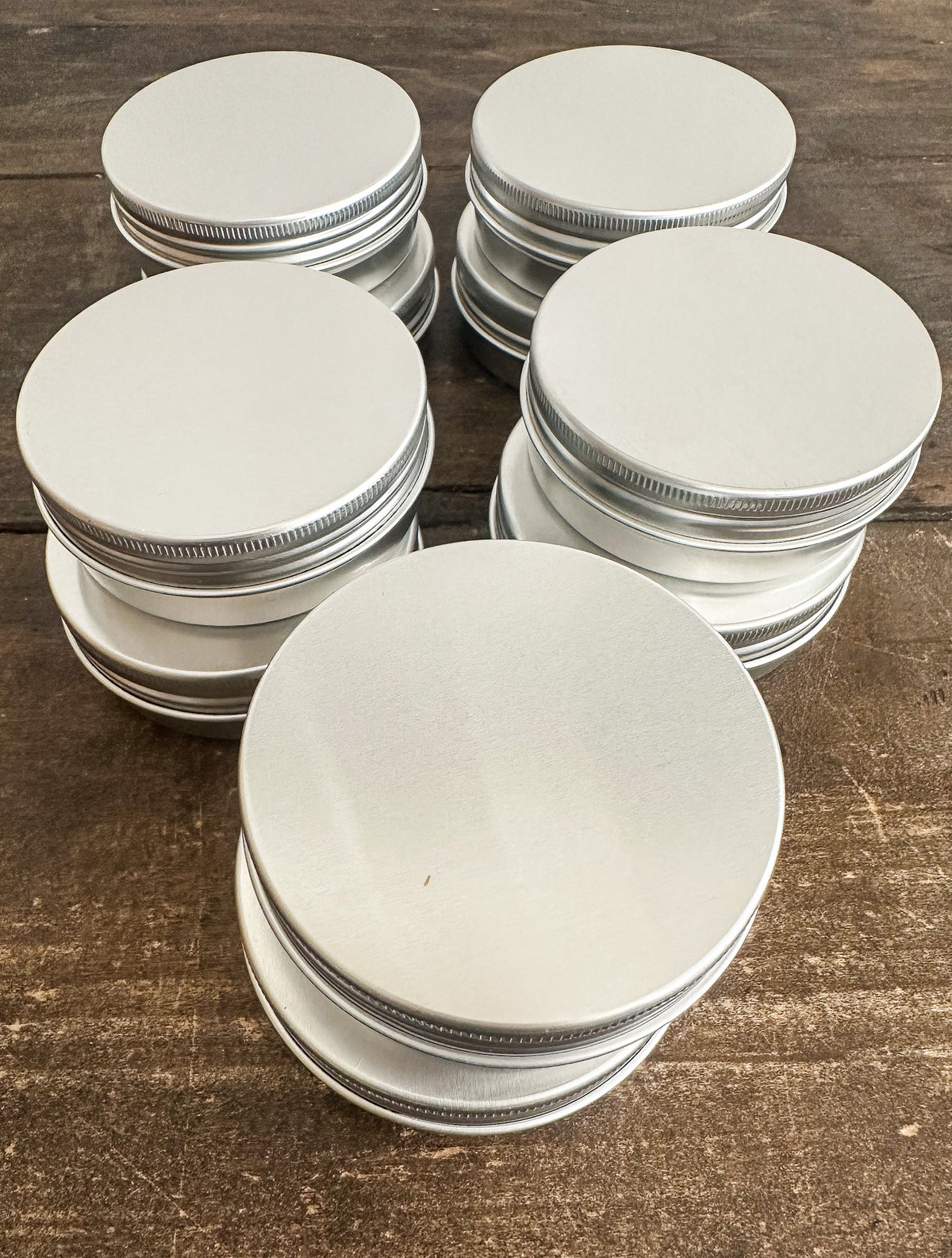 Six stacks of round silver metal tin lids with ribbed screw-on edges, arranged on a dark brown wooden surface.