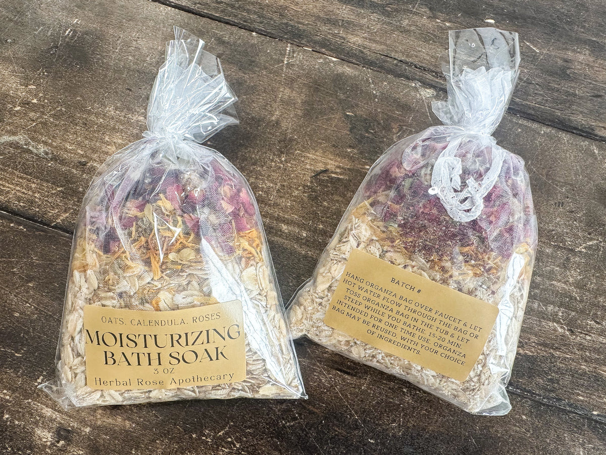 two moisturizing bath soaks packaged in a clear bag and labeled lying on a wooden surface from herbal rose apothecary