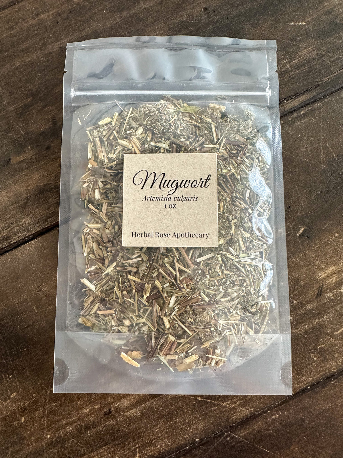 dried mugwort packaged up into a clear resealable 1oz bag on a wooden surface