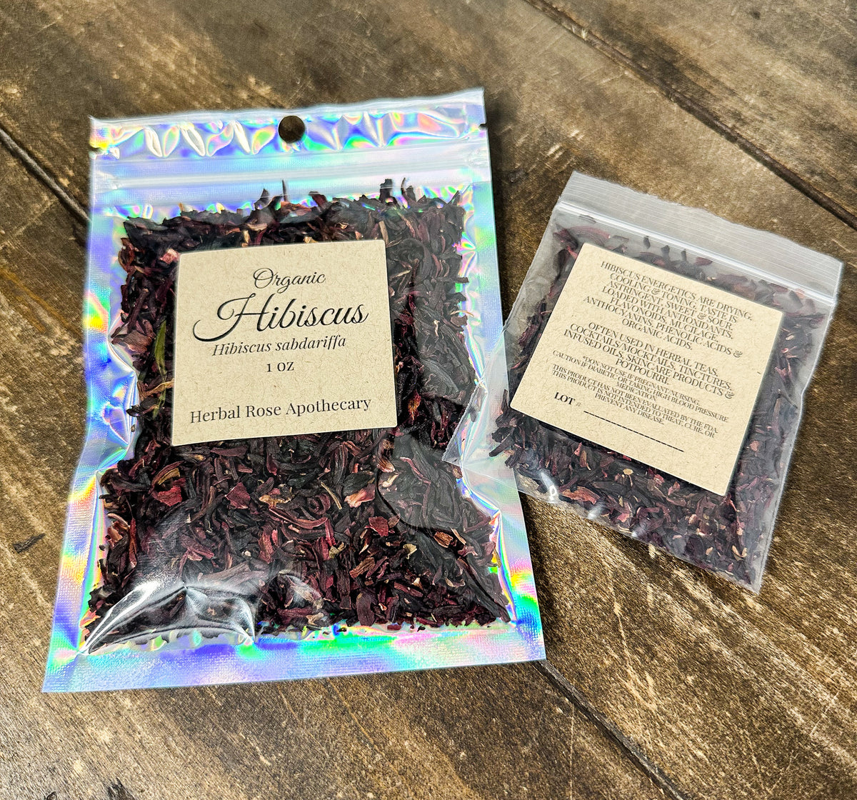 Two small resealable pouches of dried organic hibiscus tea leaves on a rustic wooden surface from herbal rose apothecary