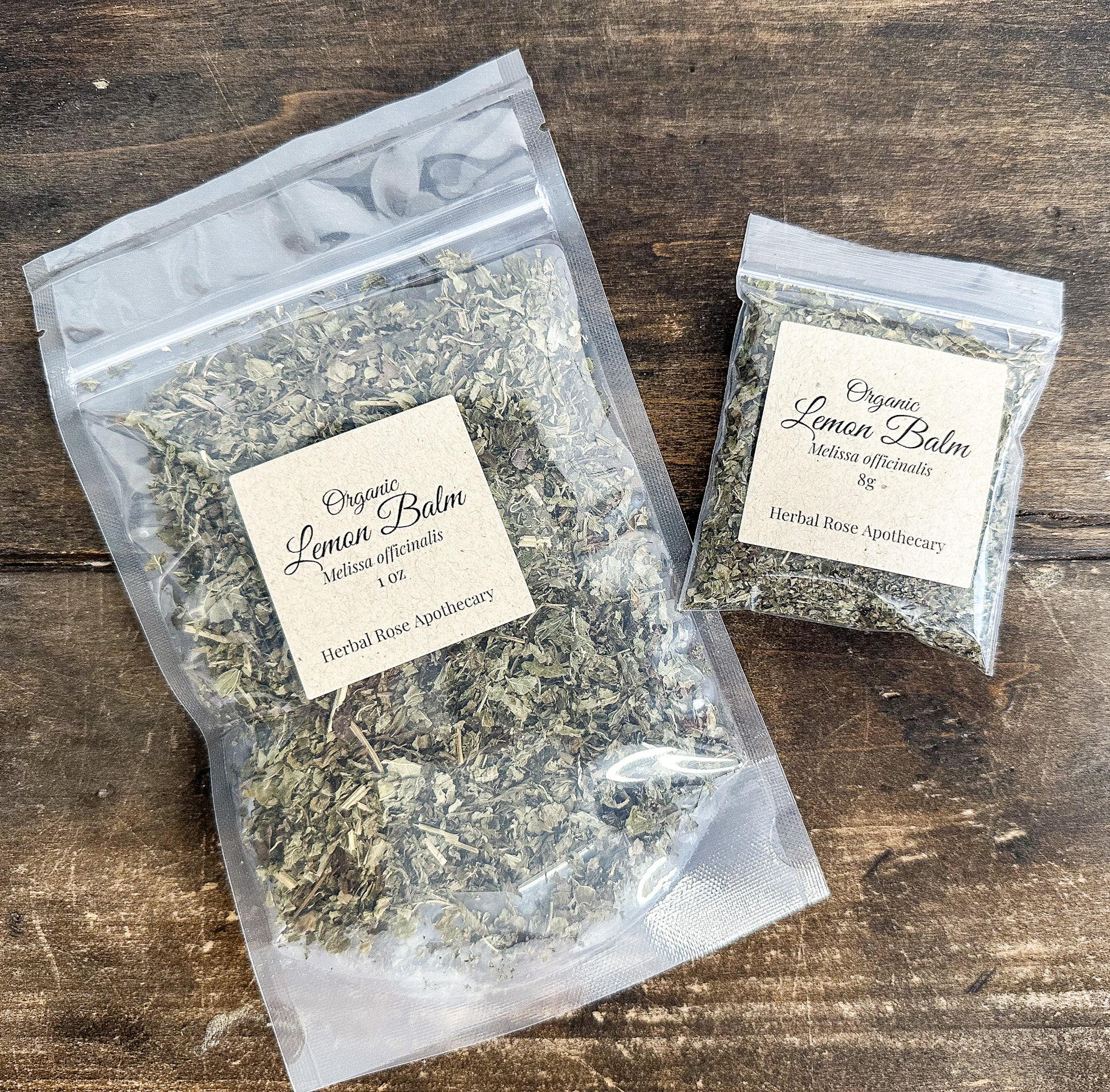 two packages of dried organic lemon balm leaves in clear bags from herbal rose apothecary on wooden surface