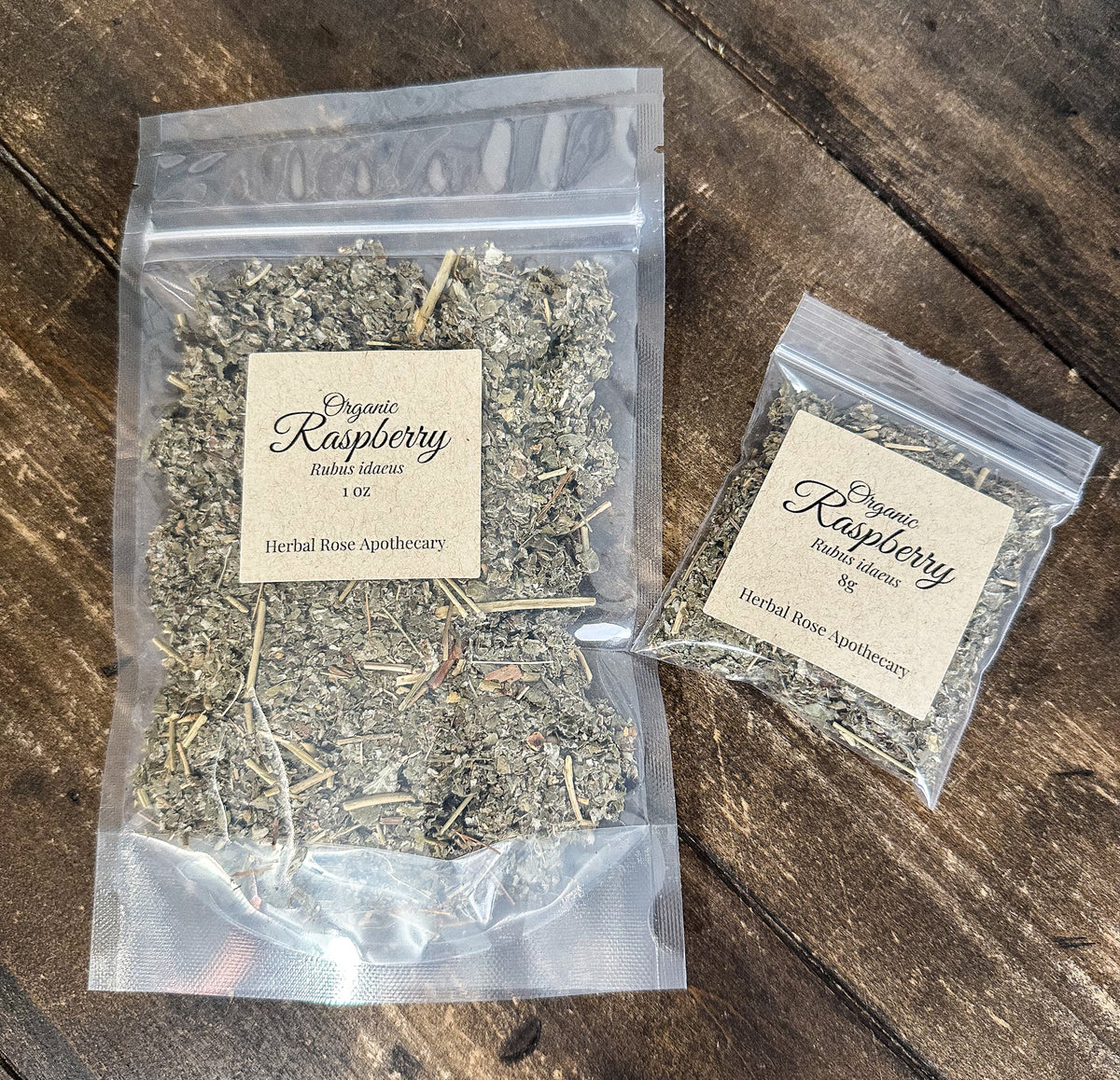 two packages of dried organic raspberry leaves in clear resealable bags from herbal rose apothecary on a wooden surface