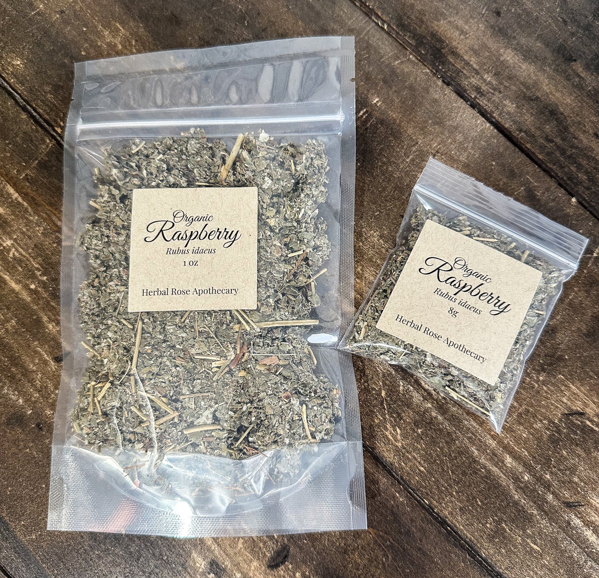 two packages of dried organic raspberry leaves in clear resealable bags from herbal rose apothecary on a wooden surface
