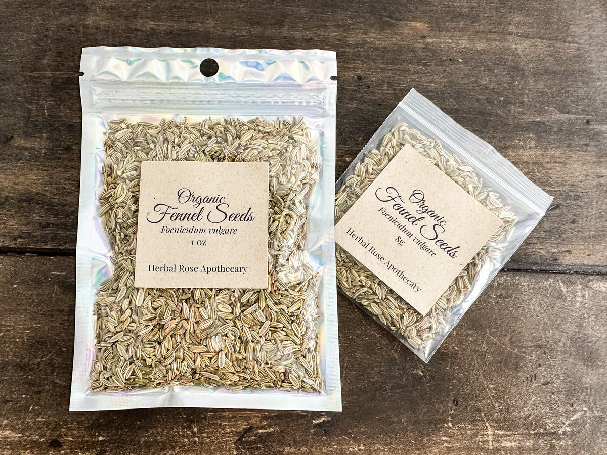 Two clear resealable pouches of Organic Fennel Seeds from Herbal Rose Apothecary, one larger 1 oz pouch and one smaller 16g pouch, displayed on a dark rustic wooden background.
