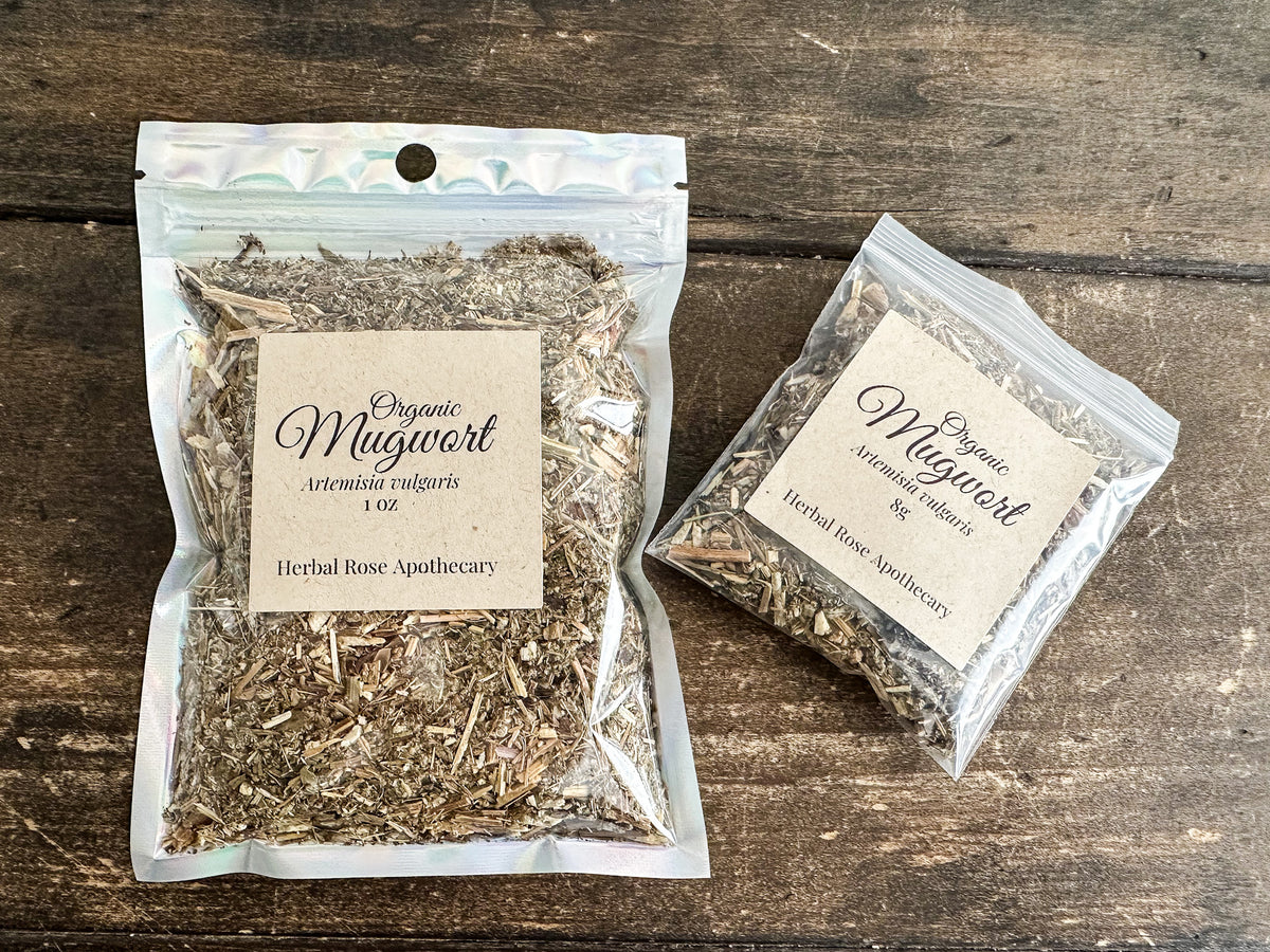 Two clear resealable pouches of Organic Mugwort herbal tea by Herbal Rose Apothecary, displayed on a dark rustic wooden background.