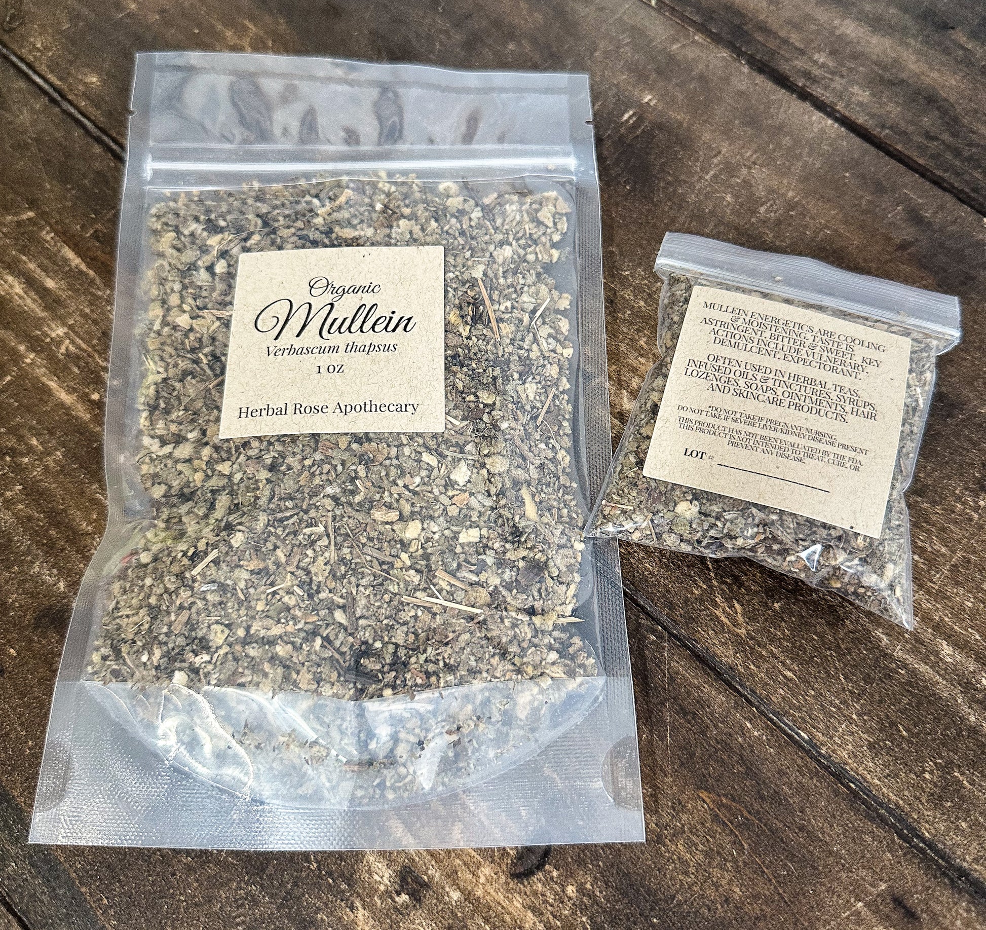 Two clear plastic bags of dried herbs on a rustic dark wood surface. The larger bag on the left is labeled 'Organic Mullein' by Herbal Rose Apothecary, and the smaller bag on the right is labeled 