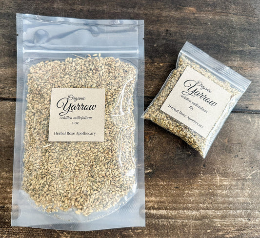 Two clear plastic bags of Organic Yarrow herbal rose apothecary seeds, one large 1 oz bag and one smaller 5 g bag, displayed on a dark rustic wooden surface.