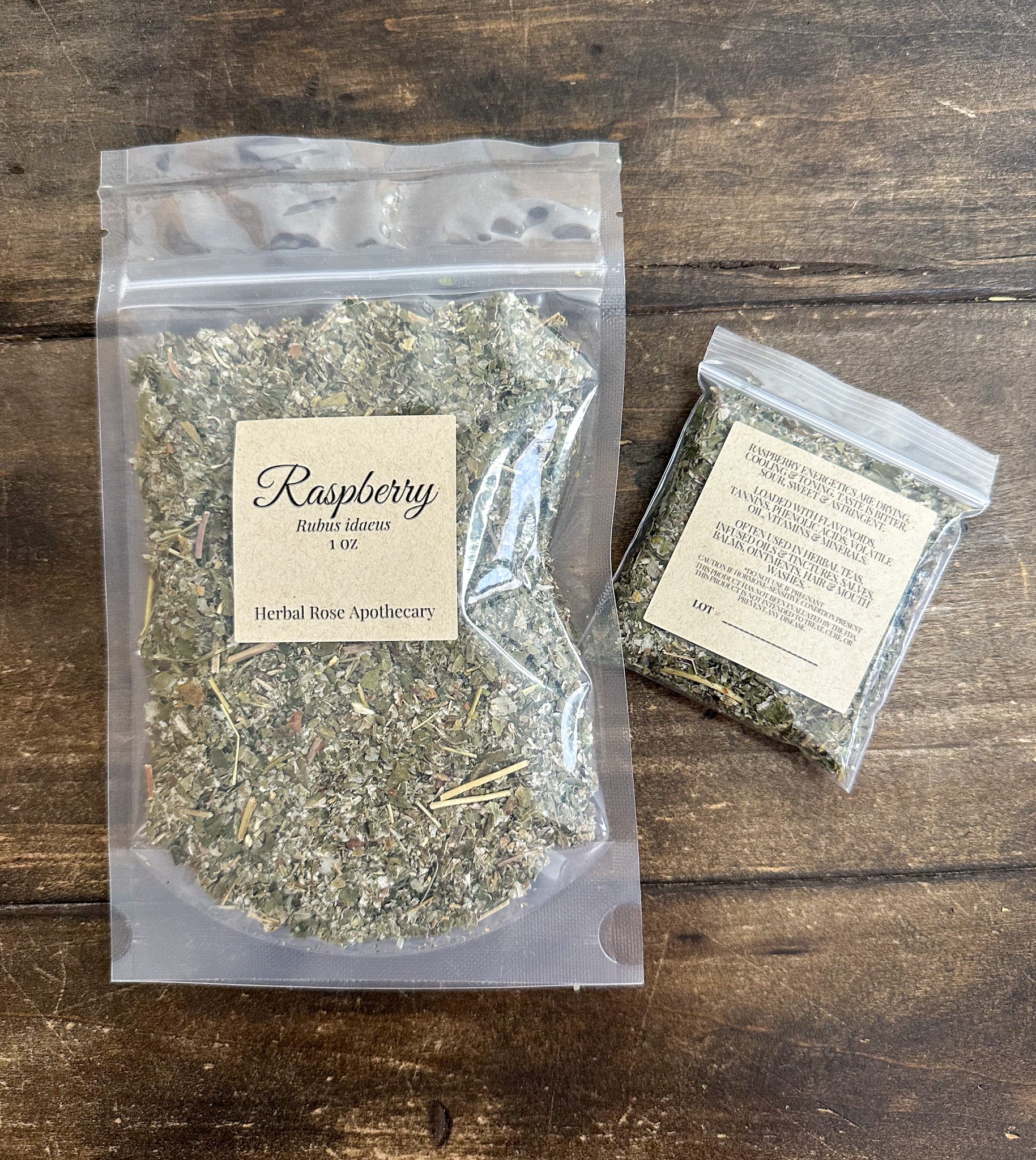 two packages of dried raspberry leaves in clear resealable bags from herbal rose apothecary on a wooden surface