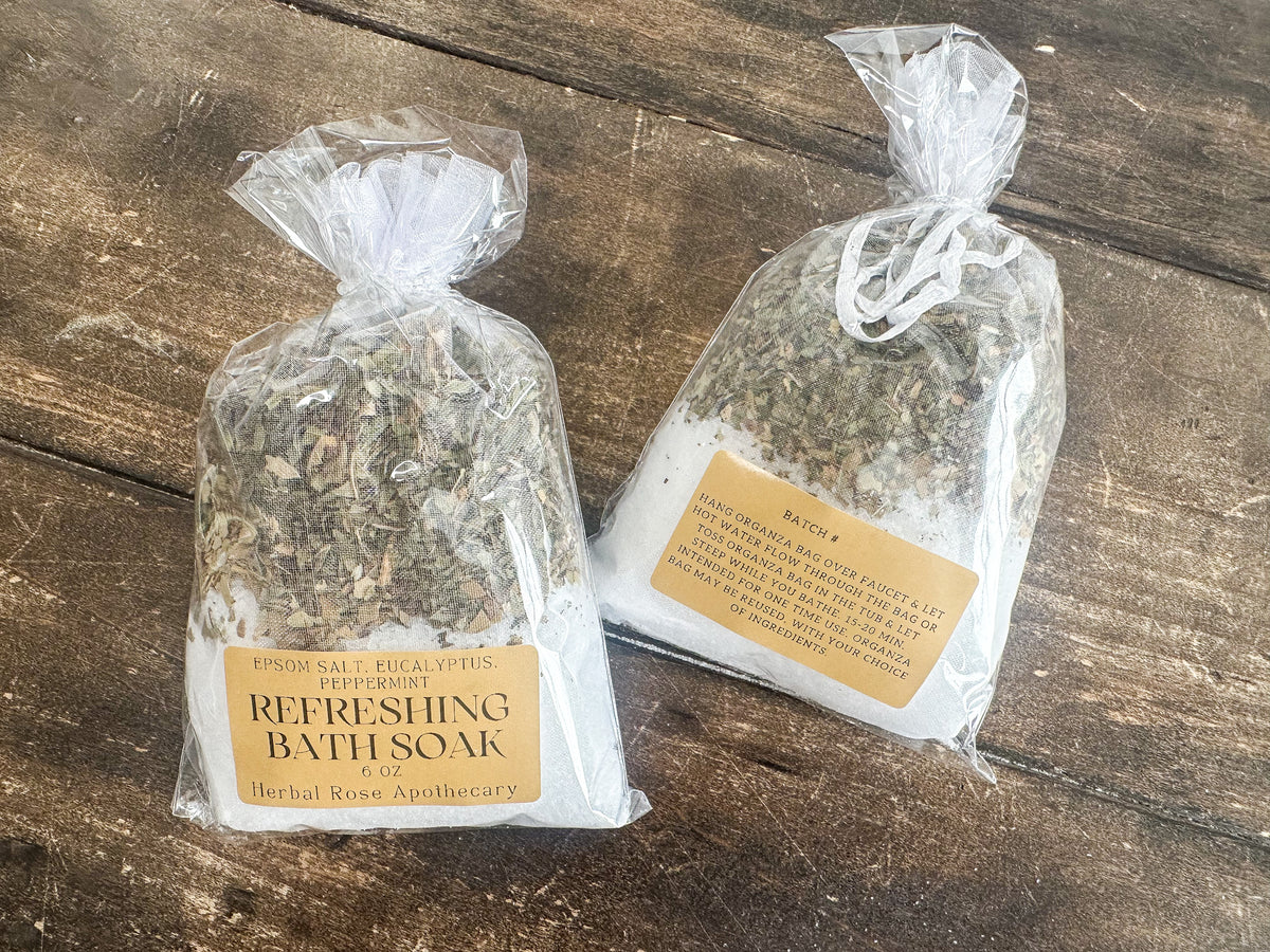 two refreshing bath soaks packaged in a clear bag and labeled lying on a wooden surface from herbal rose apothecary