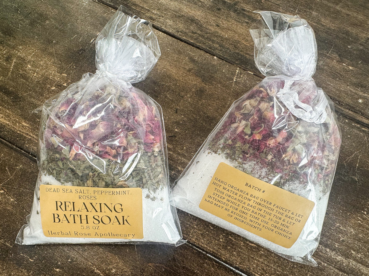 two relaxing bath soaks packaged in a clear bag and labeled lying on a wooden surface from herbal rose apothecary