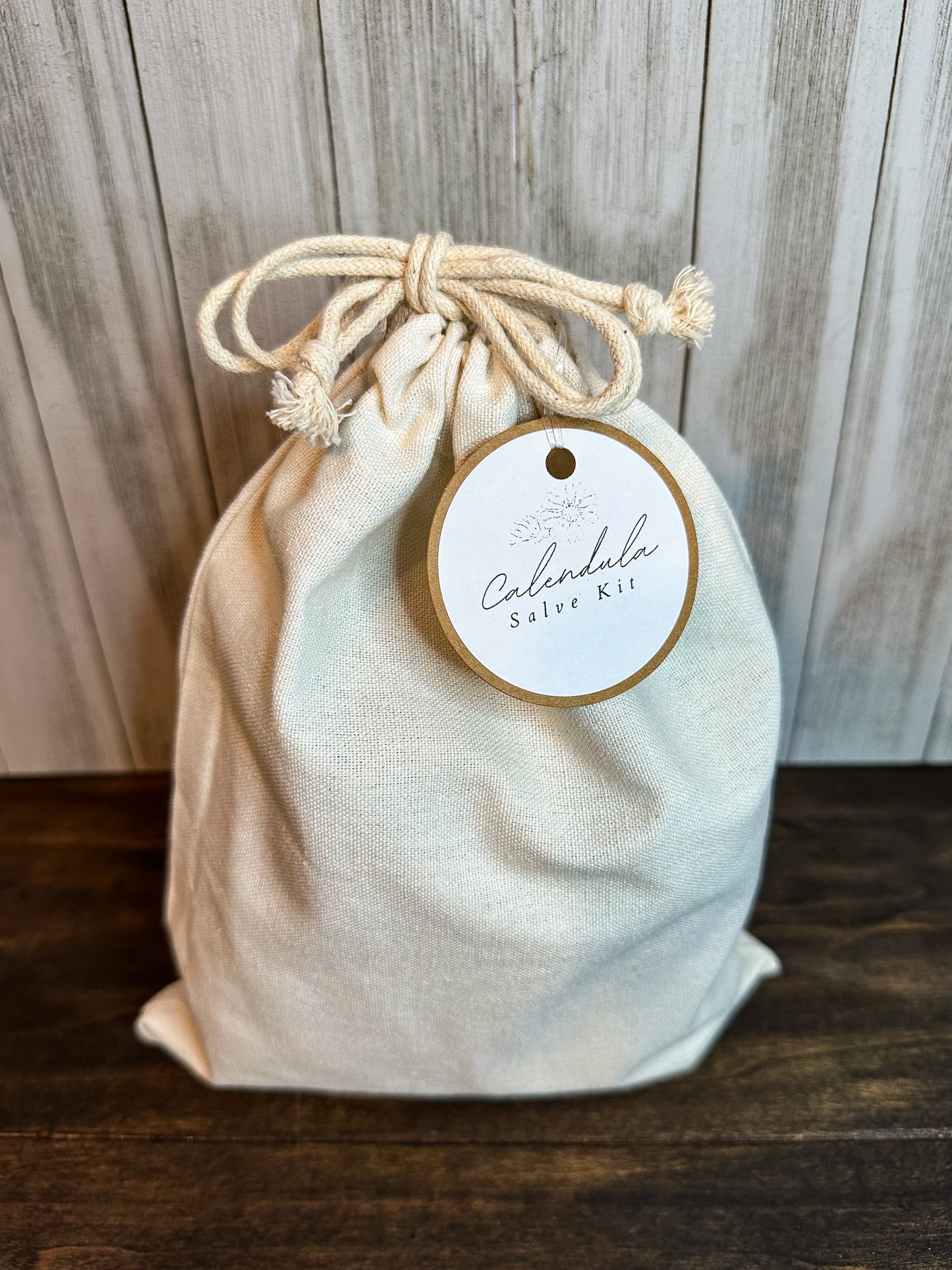 calendula salve kit in canvas bag with white and brown hang tag with grey background and wooden table