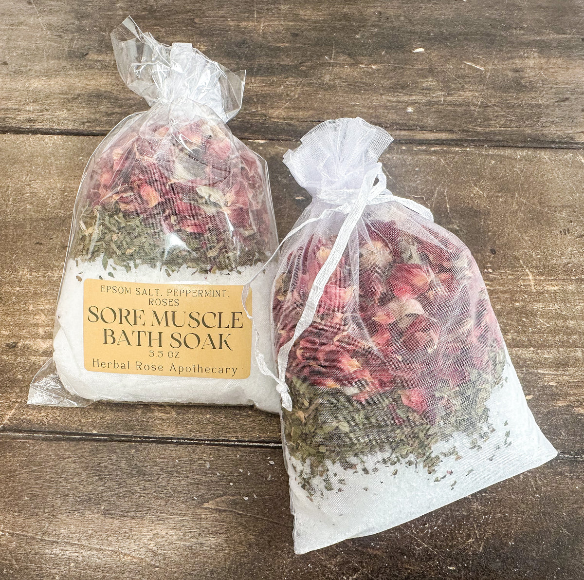 two sore muscle bath soaks packaged in a clear bag and labeled lying on a wooden surface from herbal rose apothecary