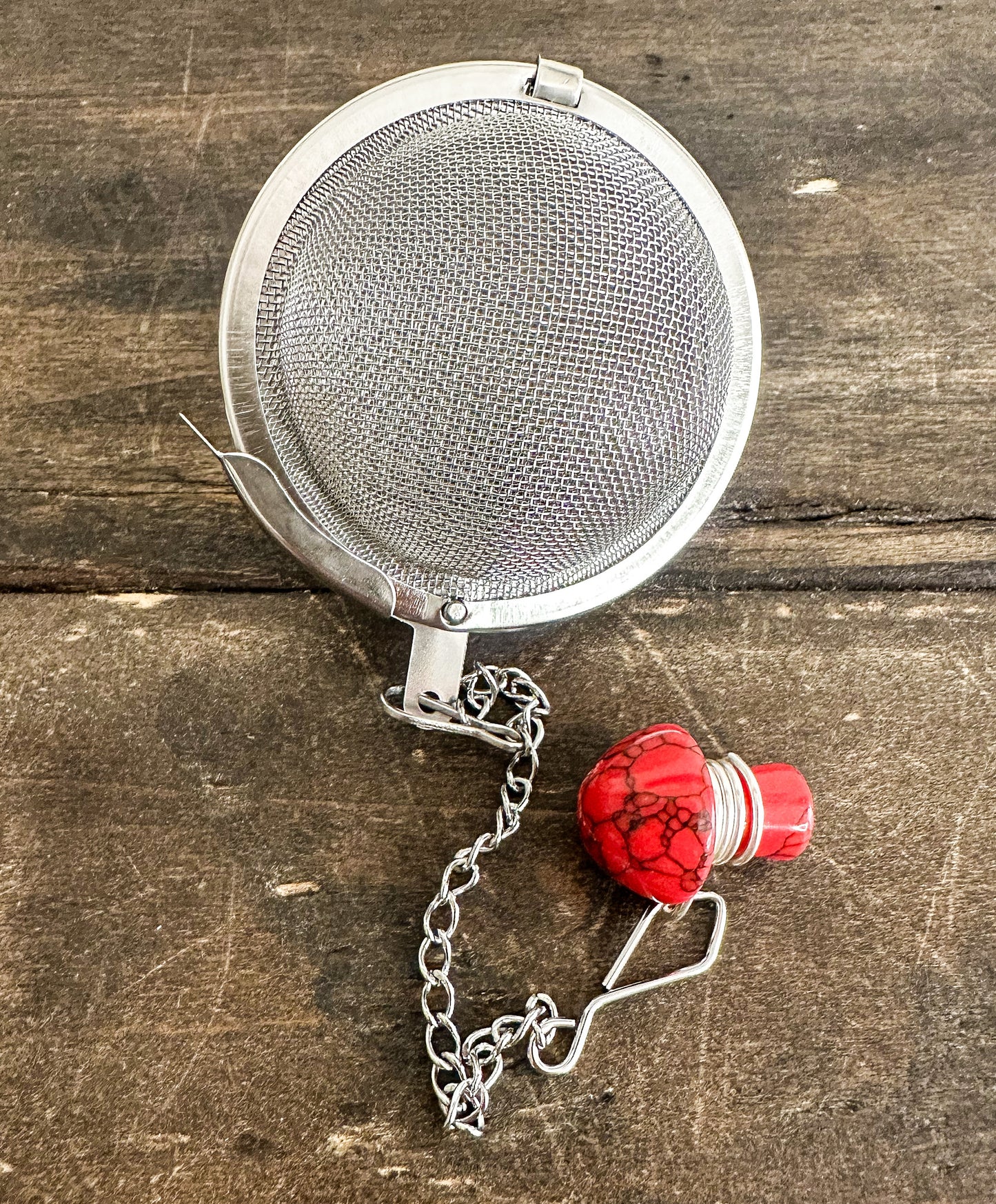 tea ball infuser with red mushroom crystal attached to tea ball infuser on wooden background