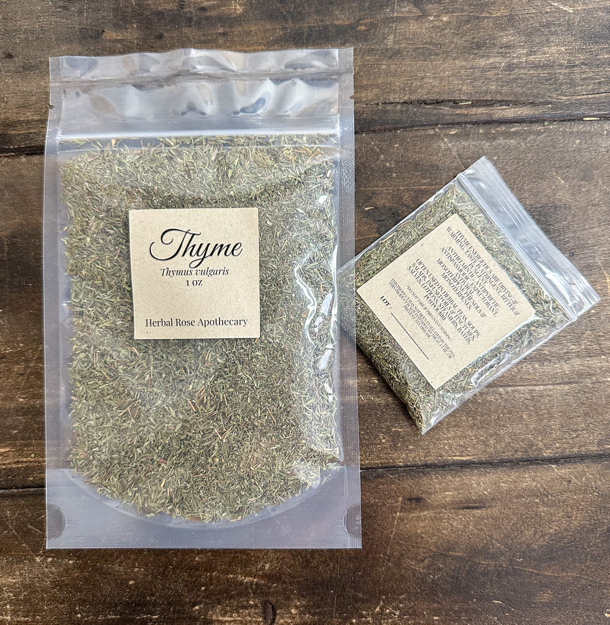 two packages of dried thyme leaves in clear resealable bags from herbal rose apothecary on a wooden surface