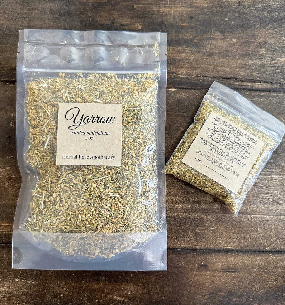two packages of dried yarrow in clear resealable bags from herbal rose apothecary on a wooden surface