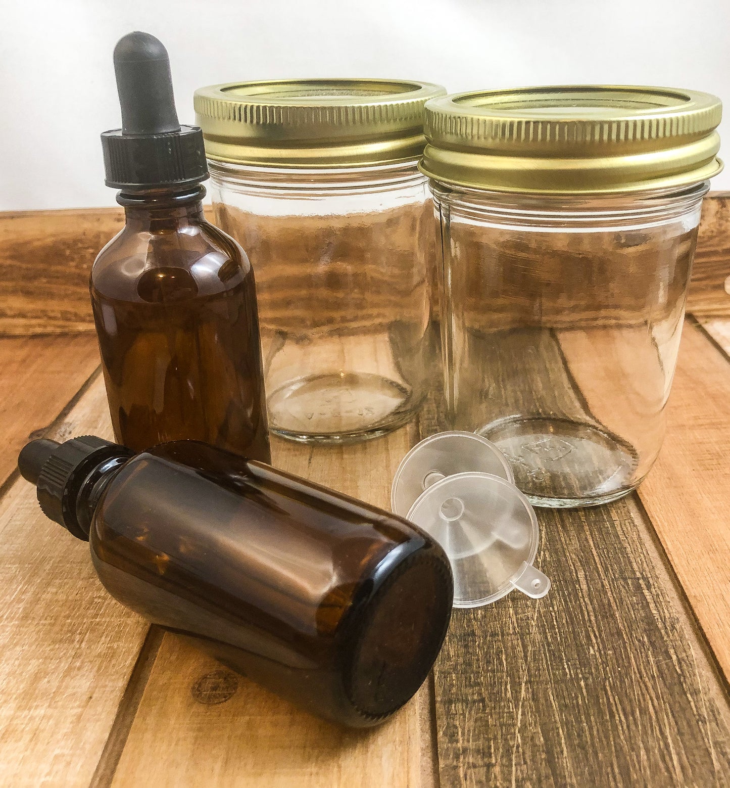 2 mason jars, 2 amber dropper bottles, 2 plastic funnels on wooden table with white background