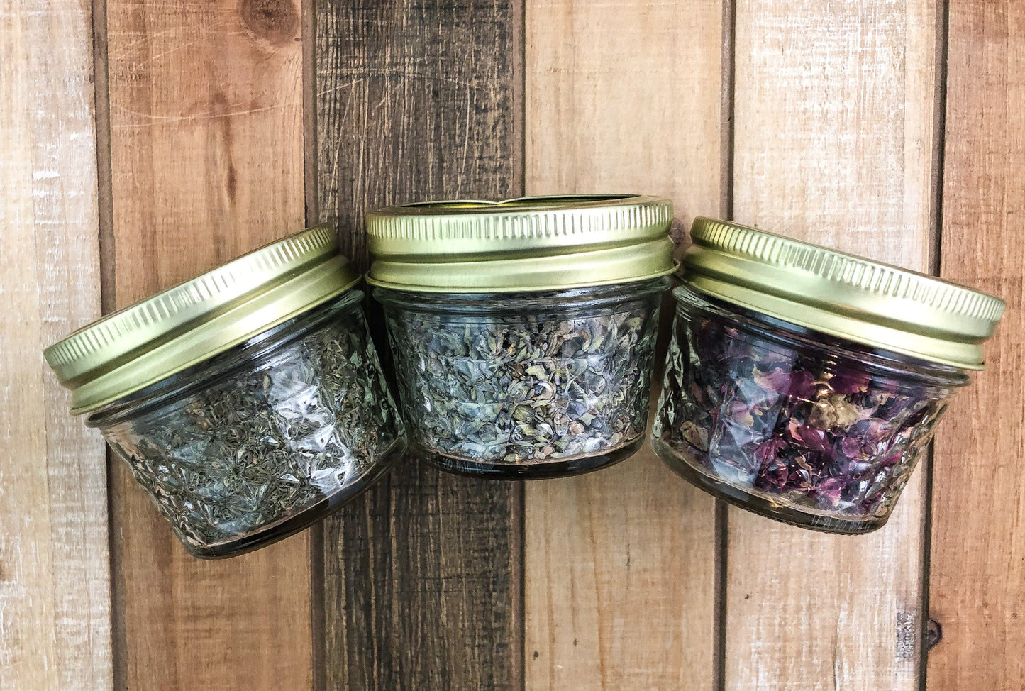 dried herbs in 3 mini glass jars on a wooden table top as background