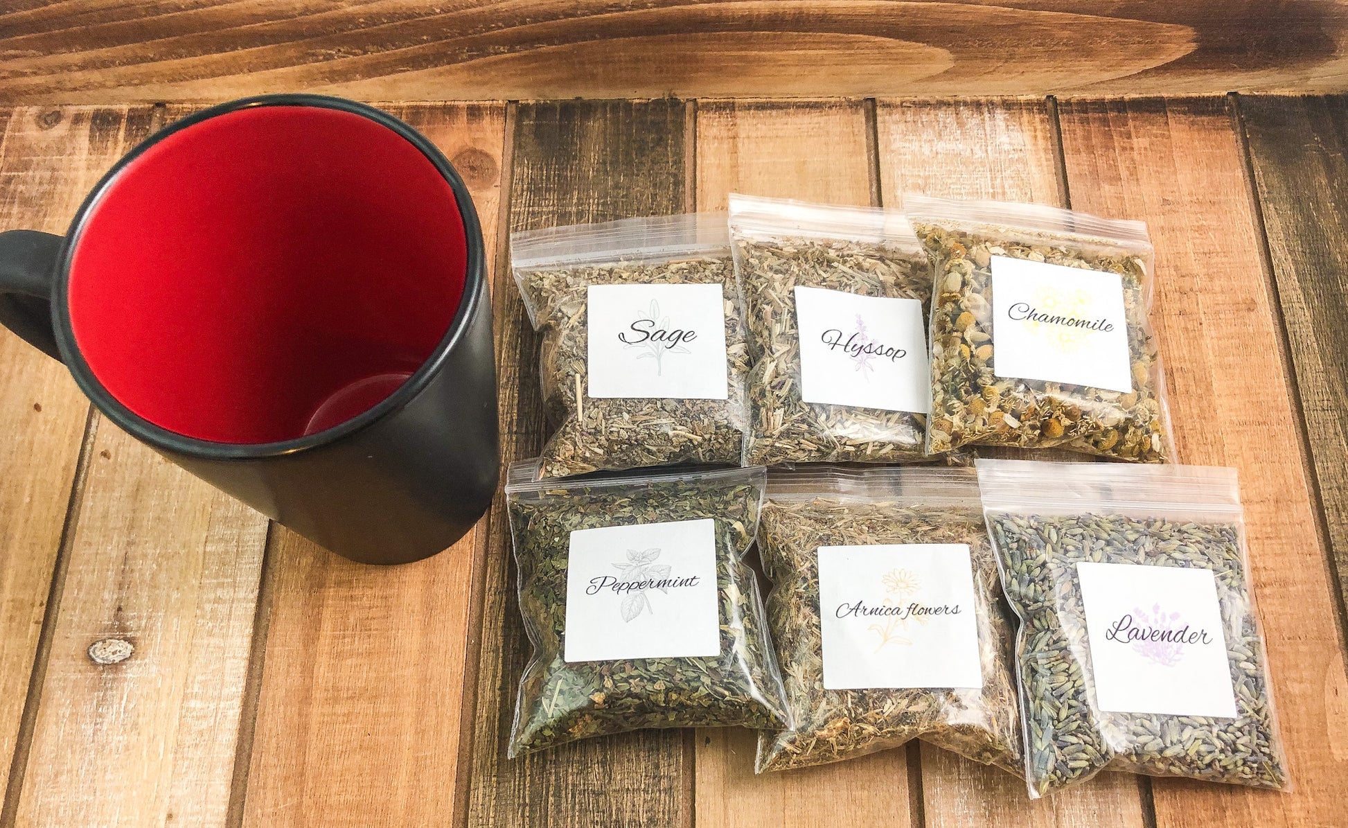 herbal sample pack; 6 8g bags of dried herbs laying next to a black and red coffee mug on a wooden table with white background